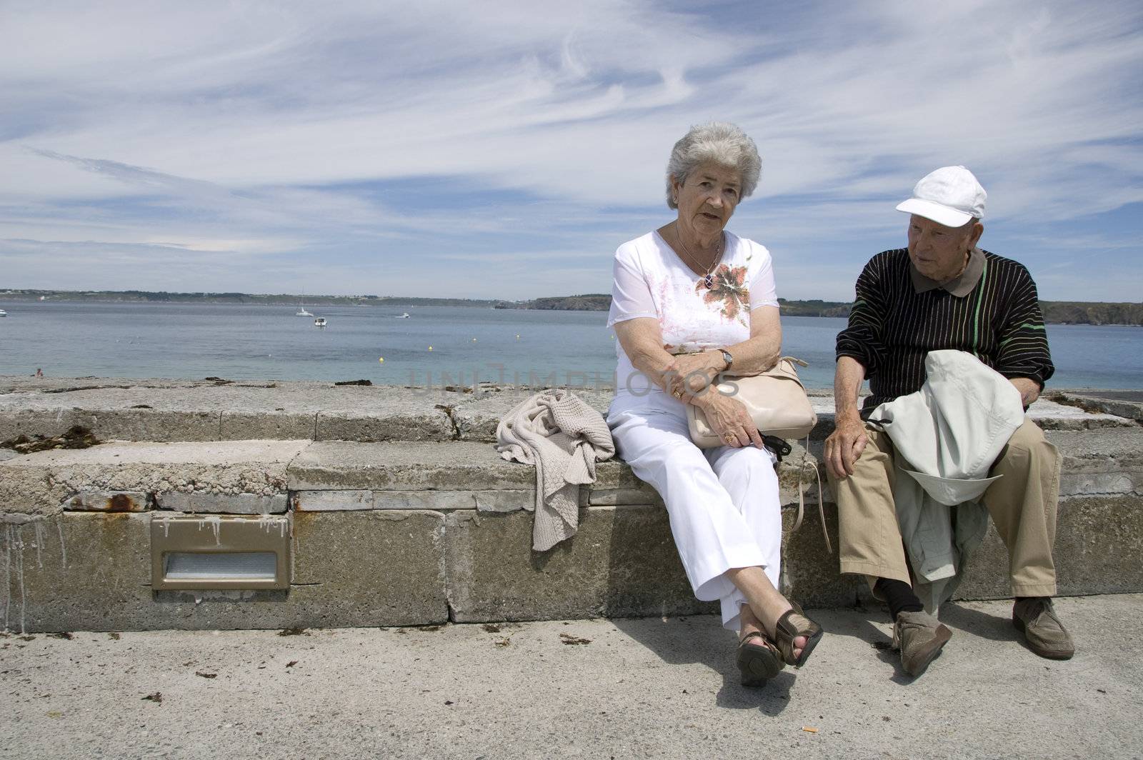 Senior couple sitting on wall in front of the atlantic ocean