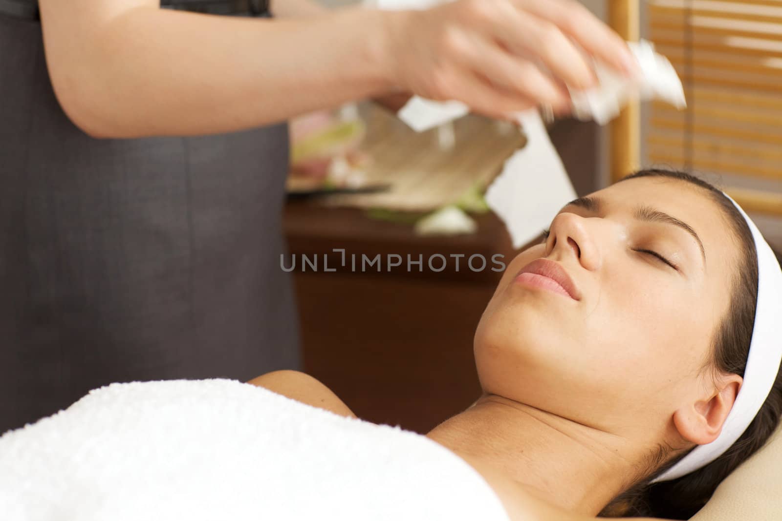 Masseuse cleaning face of young woman with tissue paper
