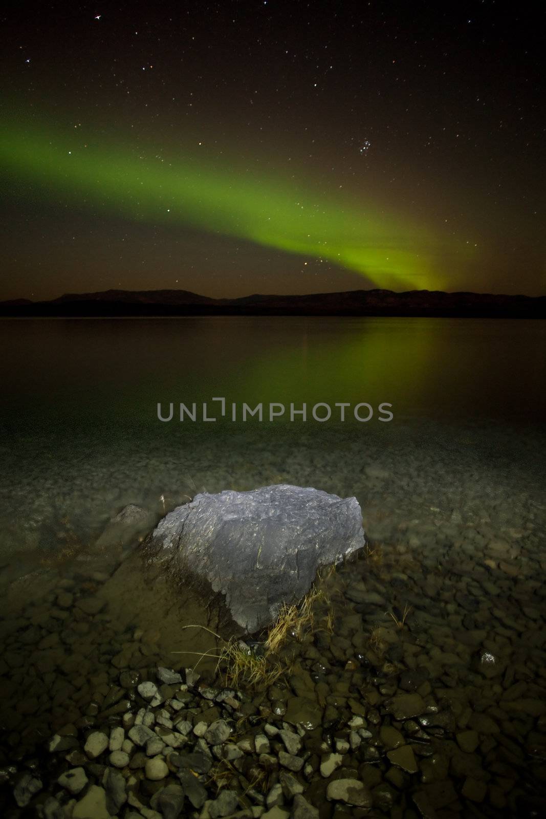 Intense northern lights (Aurora borealis) over Lake Laberge, Yukon Territory, Canada, with rock on lake shore.