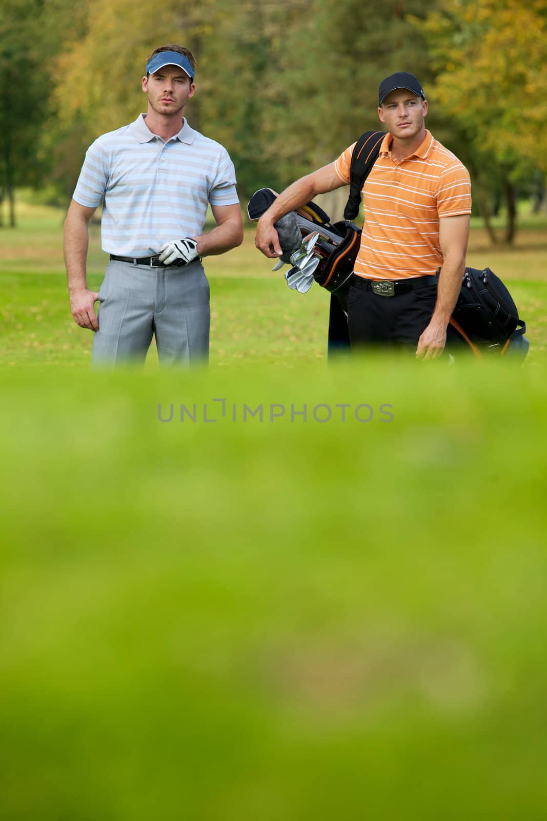 Young men standing on golf course carrying bags
