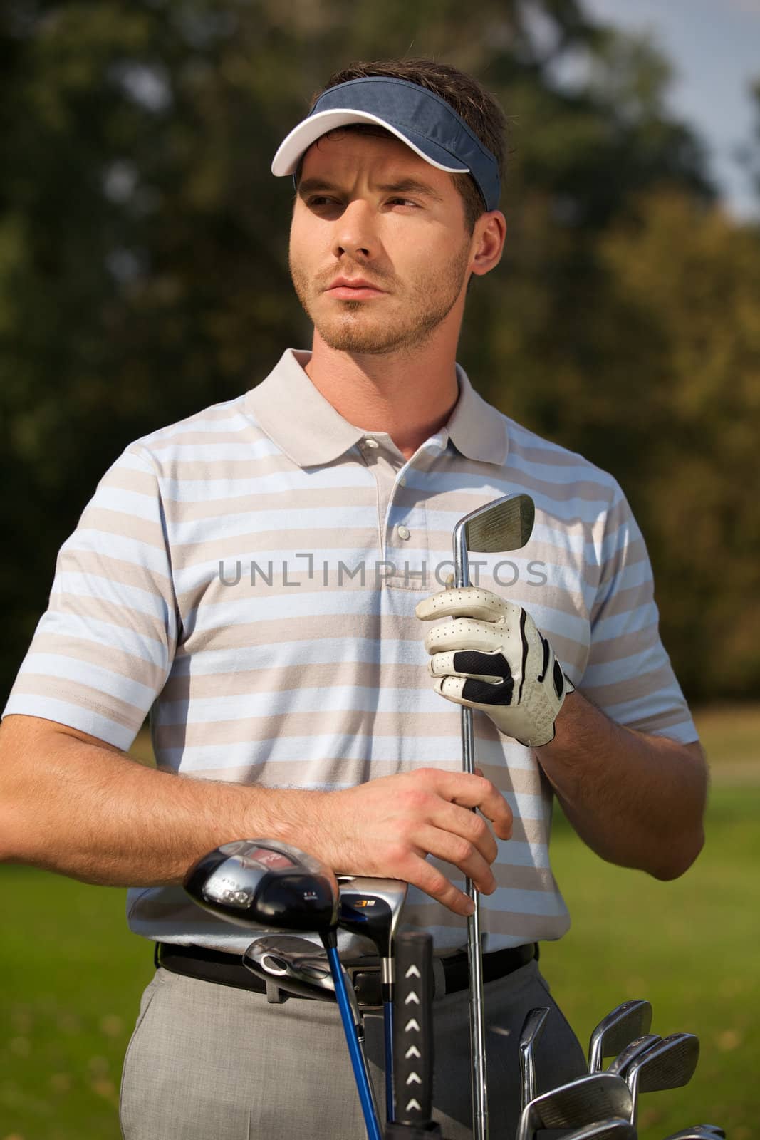 Young man standing by golf bag full of sticks