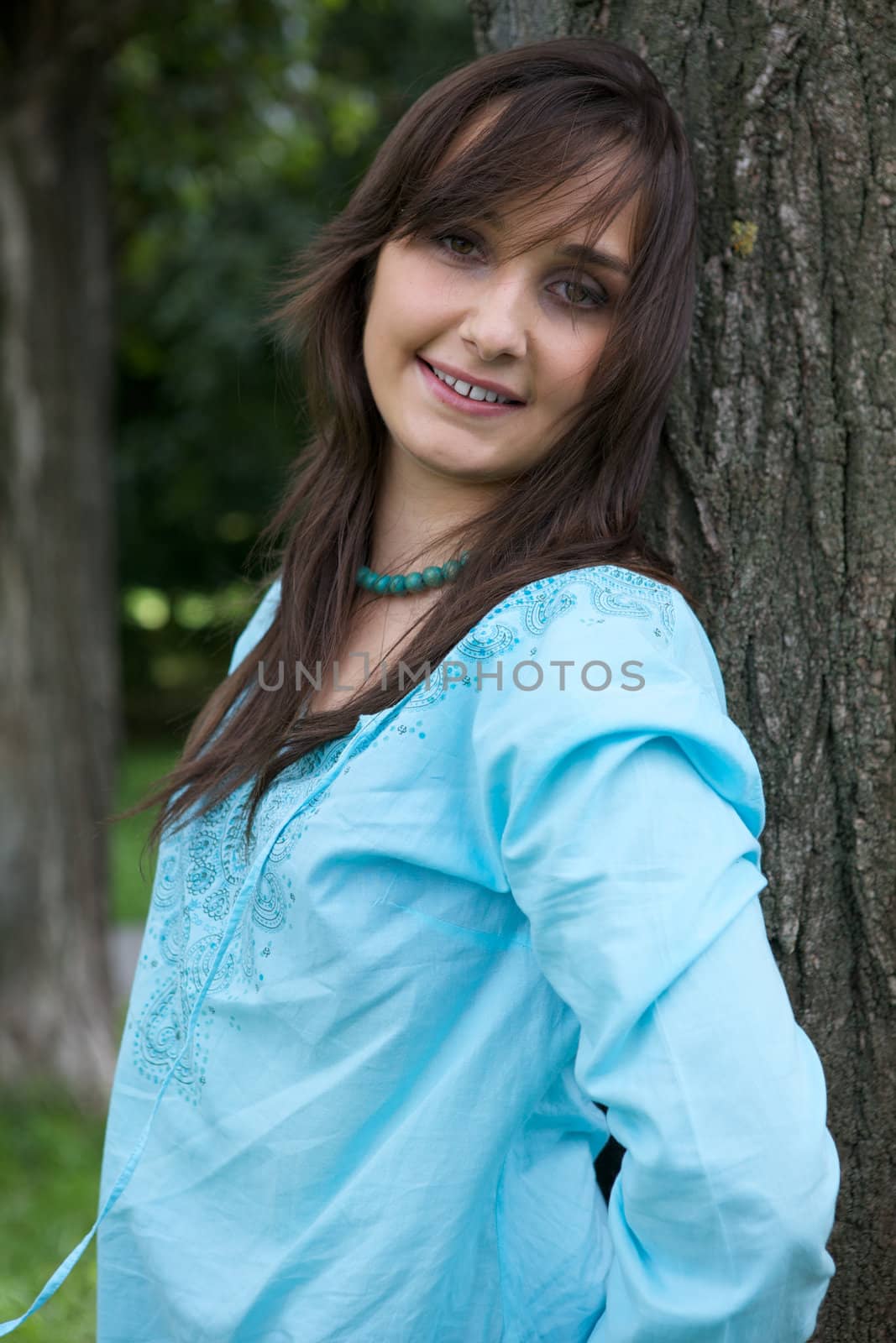 Portrait of young woman smiling by tree trunk