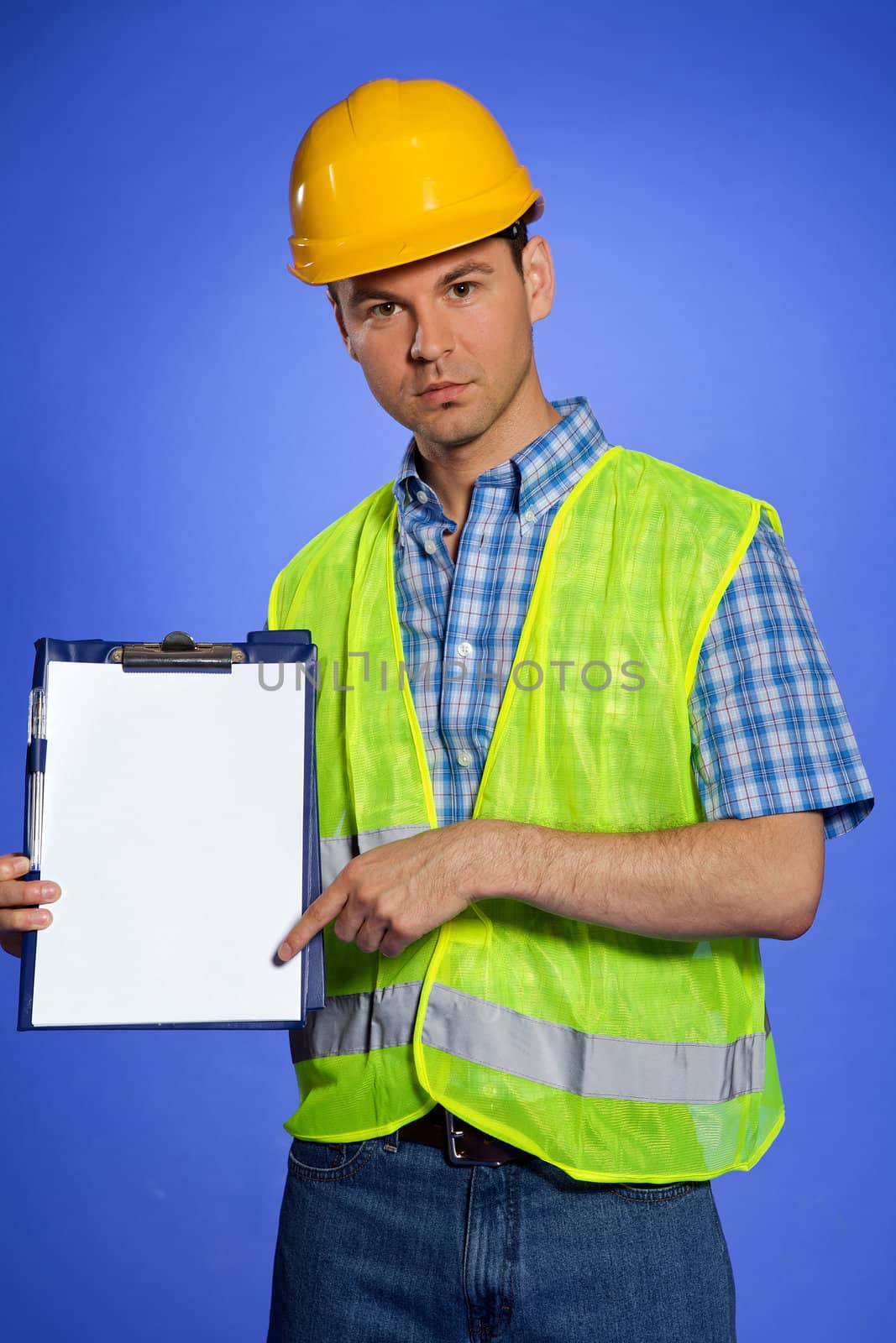 Portrait of architect in coveralls and hardhat pointing at clipboard
