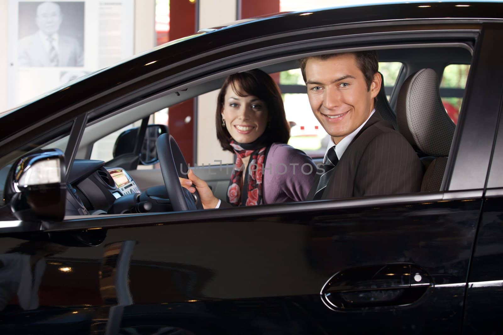 Portrait of young couple sitting in a new car at showroom