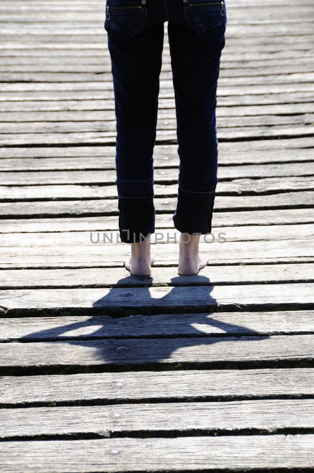 Young woman standing on wooden planks. Focus is on her shadow.