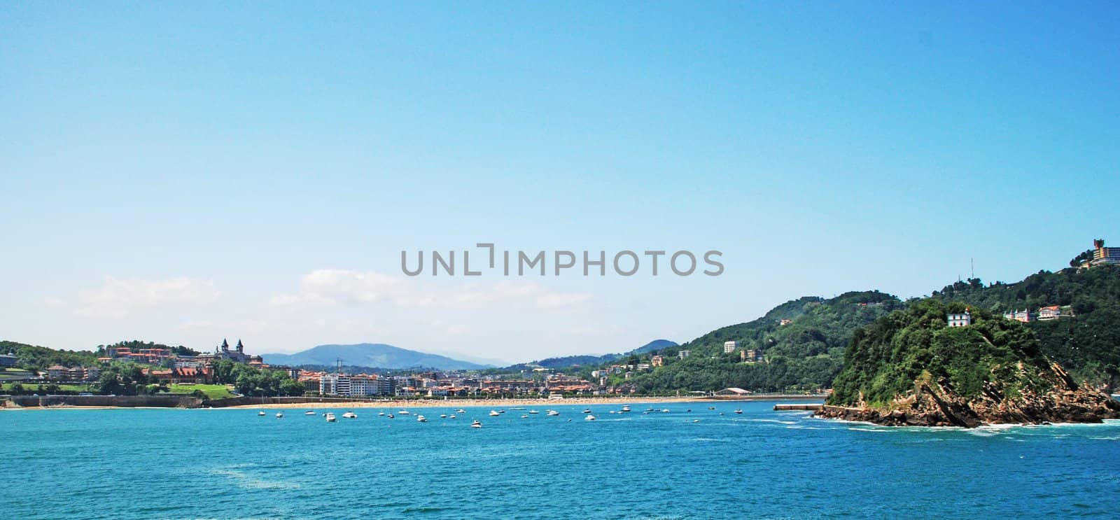 We can see a landscape in spain, a seascape, with the beach, and little islands, like big rocs; little boats, blue sky and many nature and urbanism.