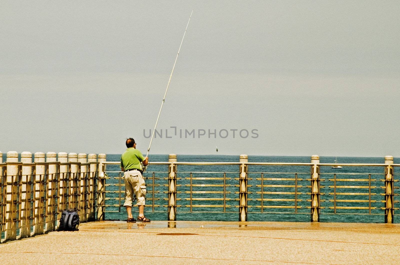 A fisherman is fishing on a bridge of san sebastian during the summer, in the background the atlantic ocean.