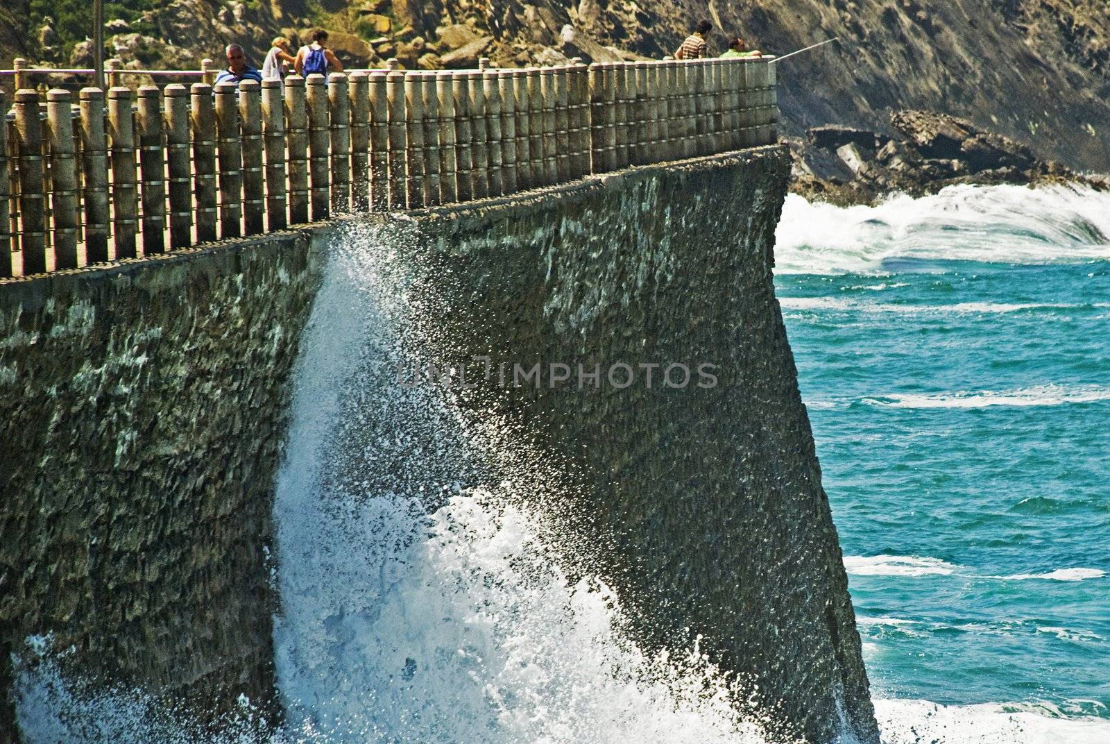 Water arrives at the border and brake up very hard against rocs. In th background we can see ocean and other rocs.