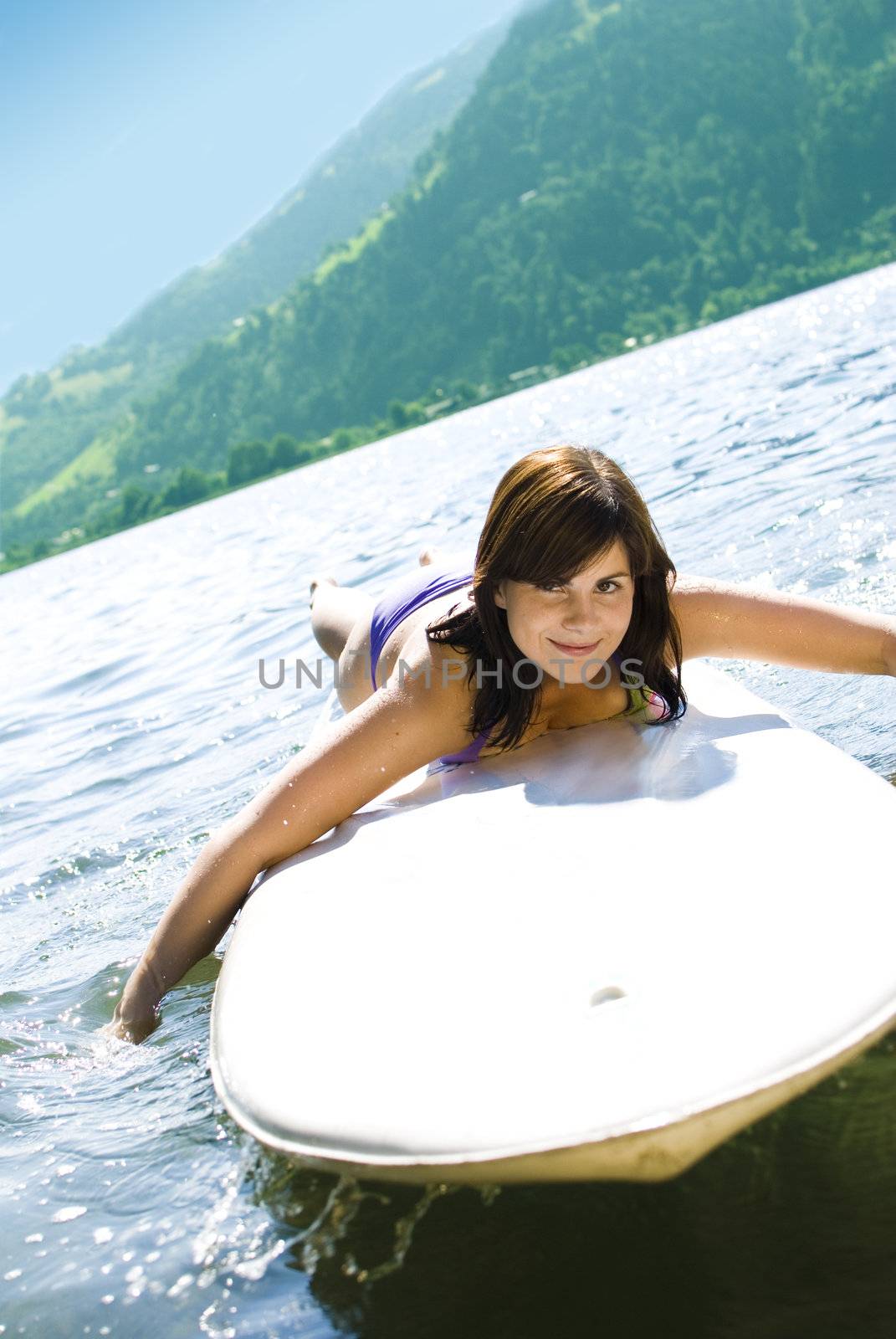 Cute girl relaxing on a surfboard in austrian lake.