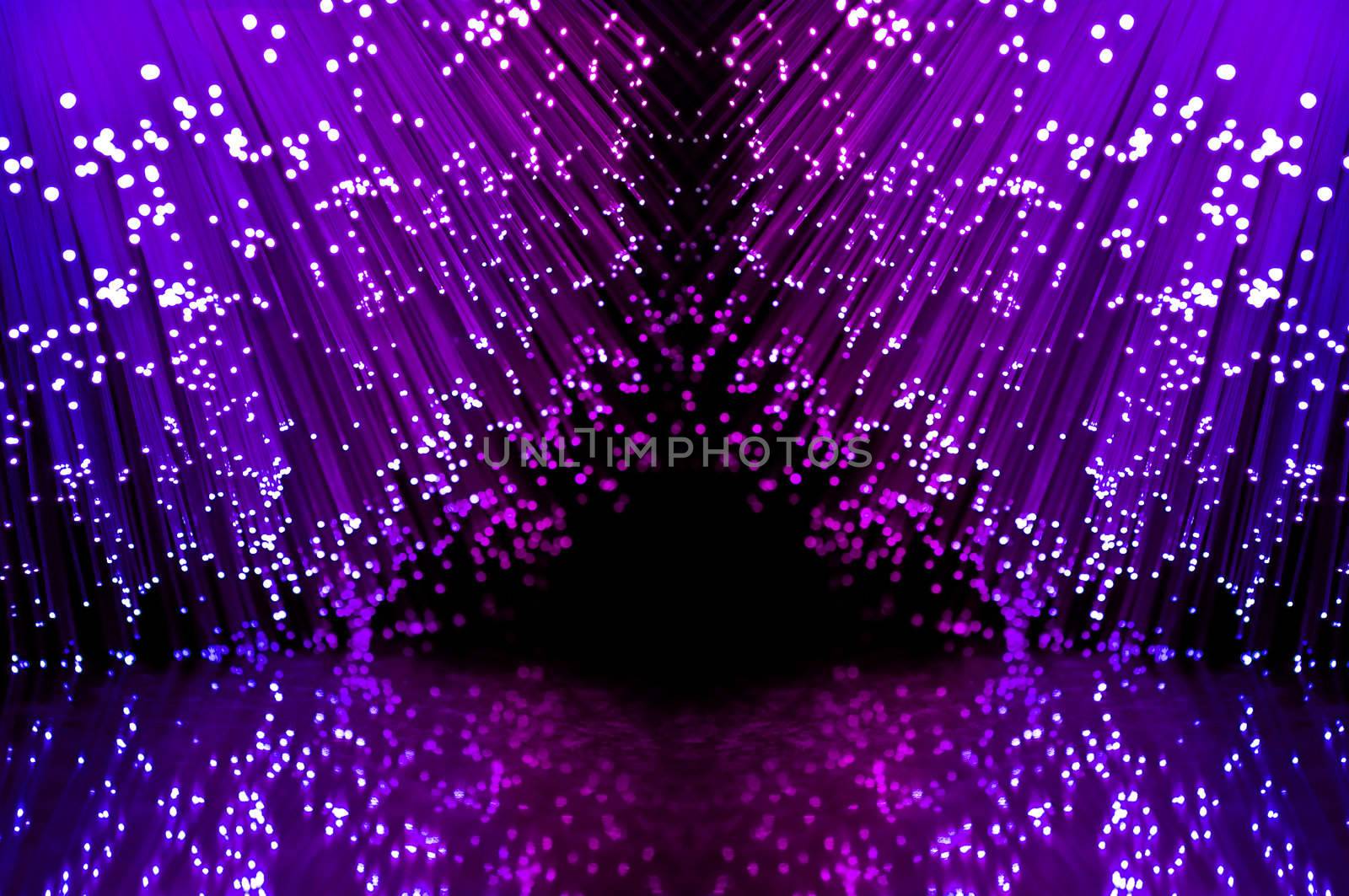 Close up on two groups of illuminated blue and magenta fiber optic light strands against a black background and reflecting into the foreground.