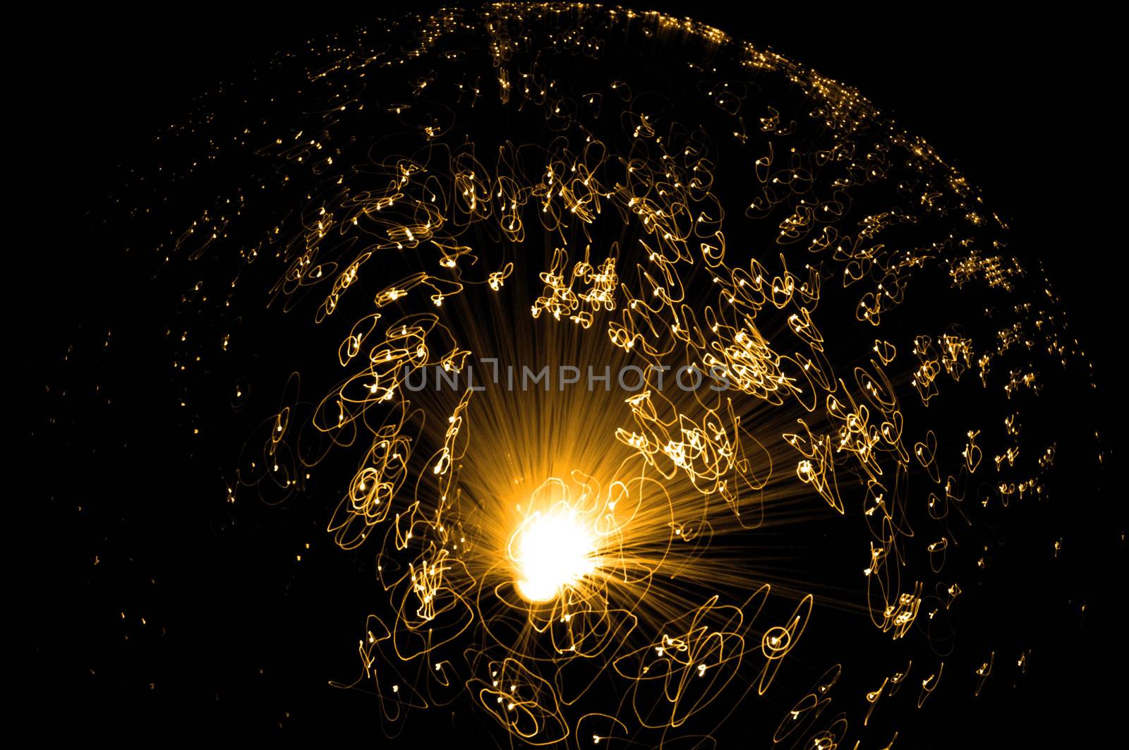 Catching the movement of the ends of many illuminated golden fiber optic strands against a black background.