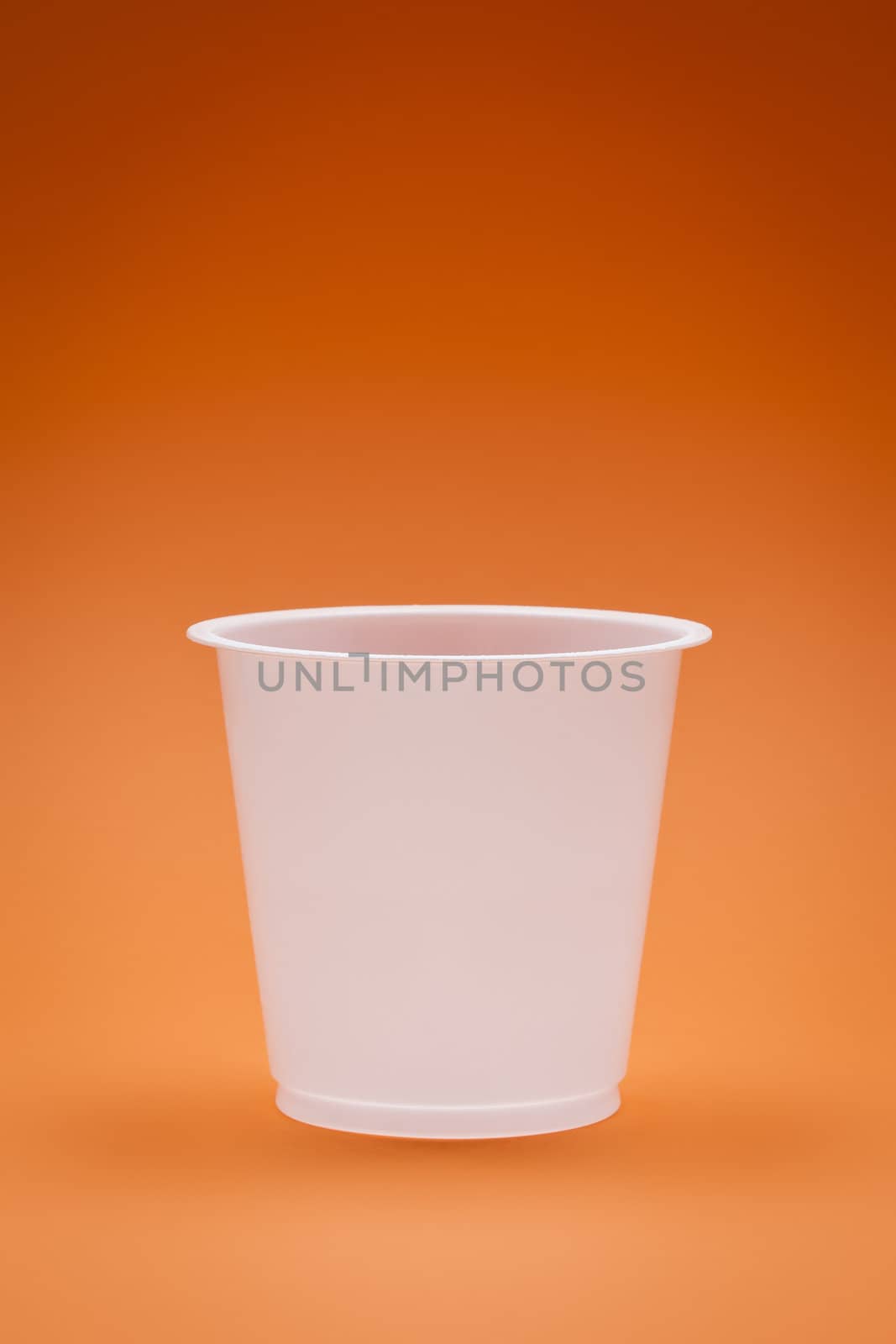 An image of a white empty plastic cup on an orange background