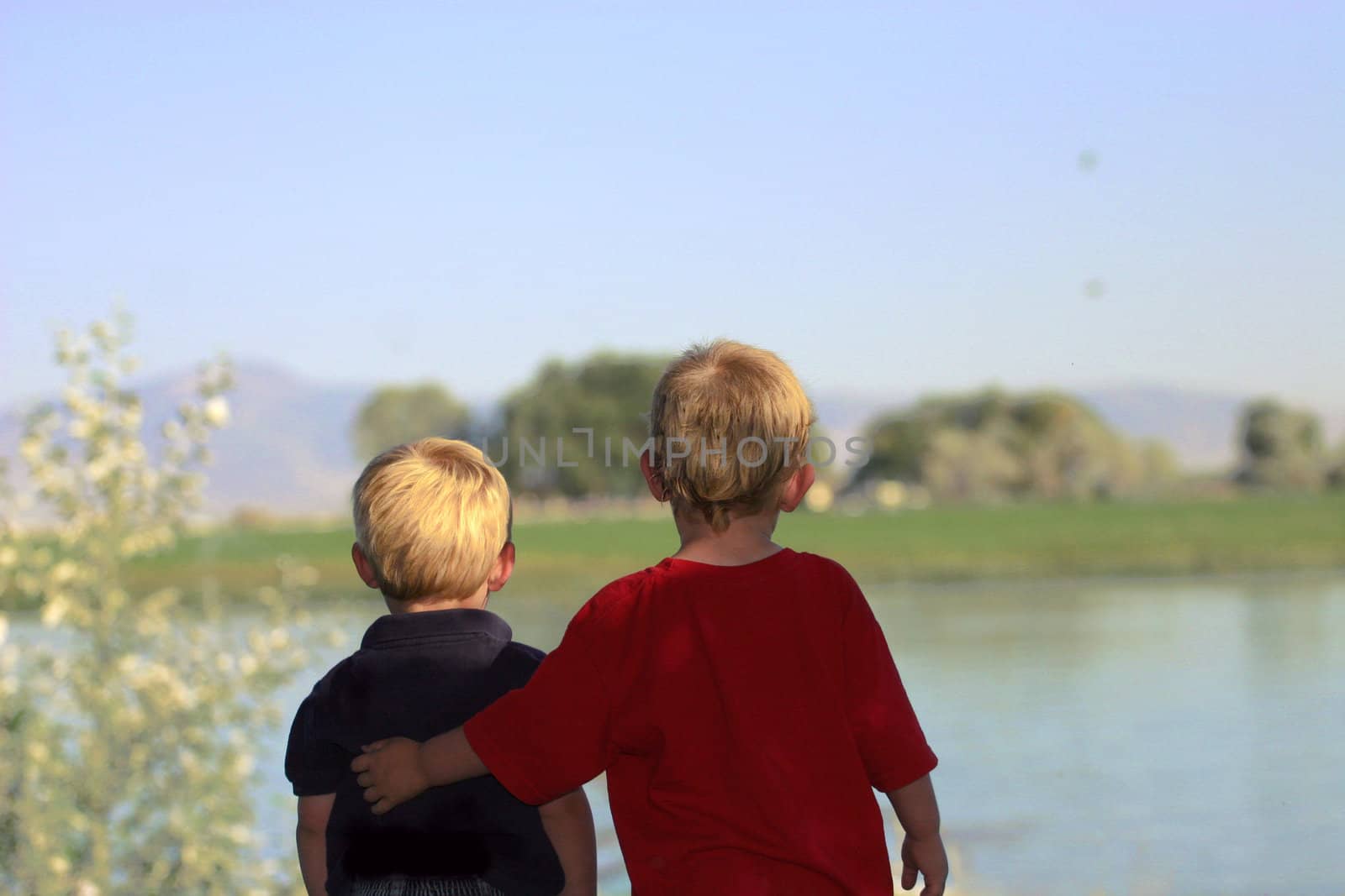 Two little brothers looking out towards water with protective arm extended.