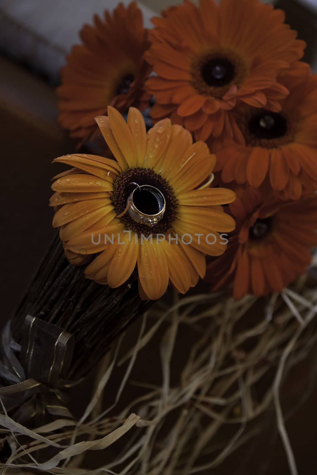 A beautiful ladies wedding ring pinned on the center of a striking orange flower among red flowers in a bouquet