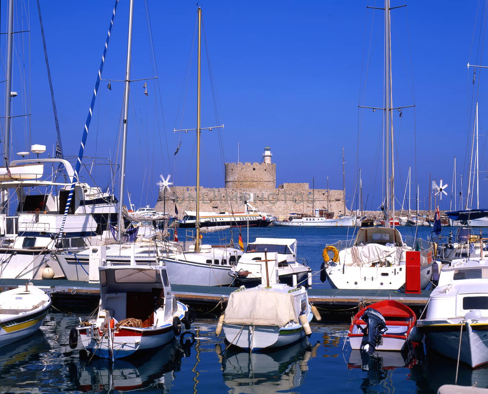 Boats moored in harbour of Rhodes, greece, with old fort in background