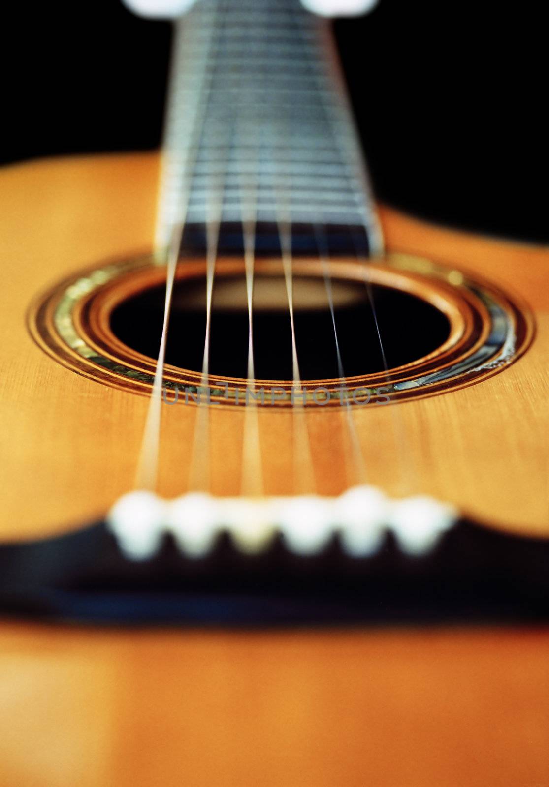 A very short depth-of-field image of an acoustic guitar from the bridge looking up the neck.
