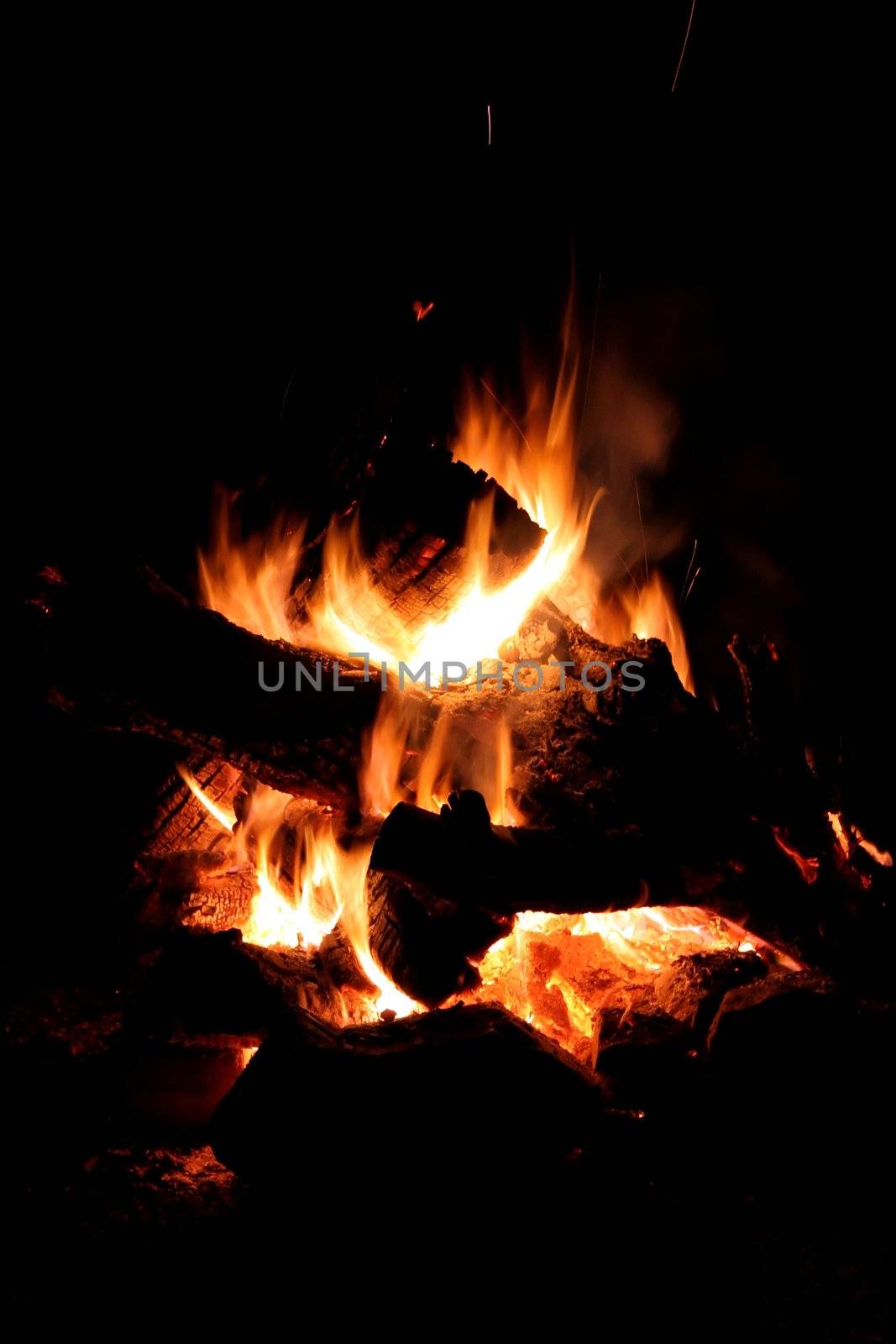 Glowing embers and flames of a camp fire at night