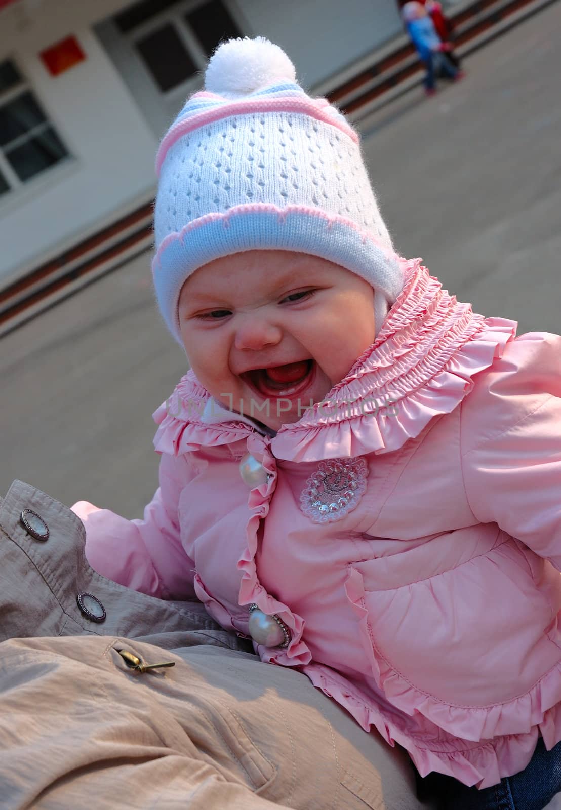 Pretty little girl in pink jacket laughing on mother's hands.