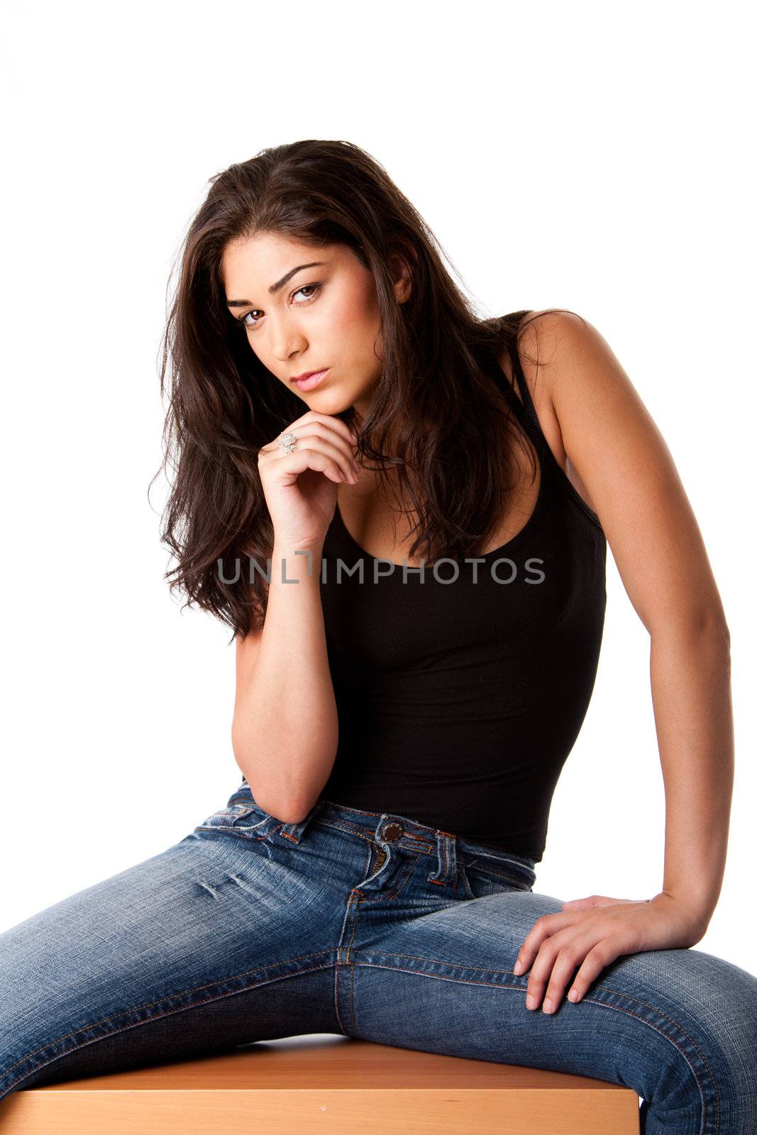 Beautiful posing fashion woman with brown long hair sitting, wearing blue denim jeans and black tank top, isolated.
