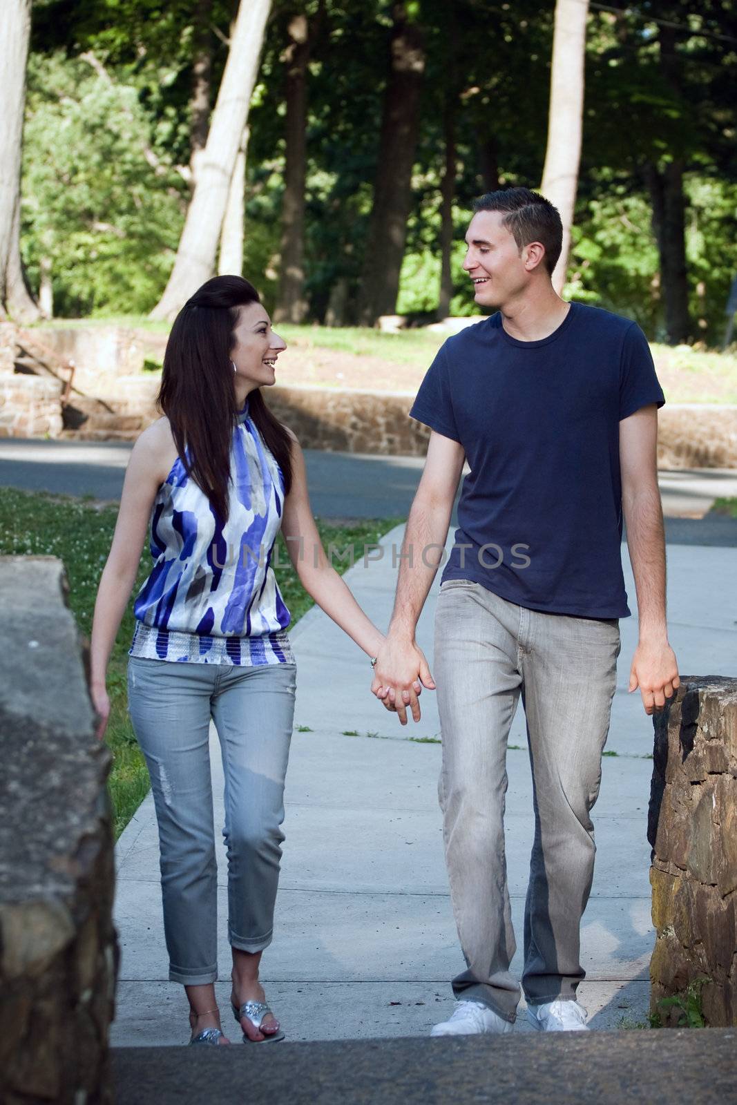 A happy young couple in their mid twenties smiling at each other during a walk through the park.