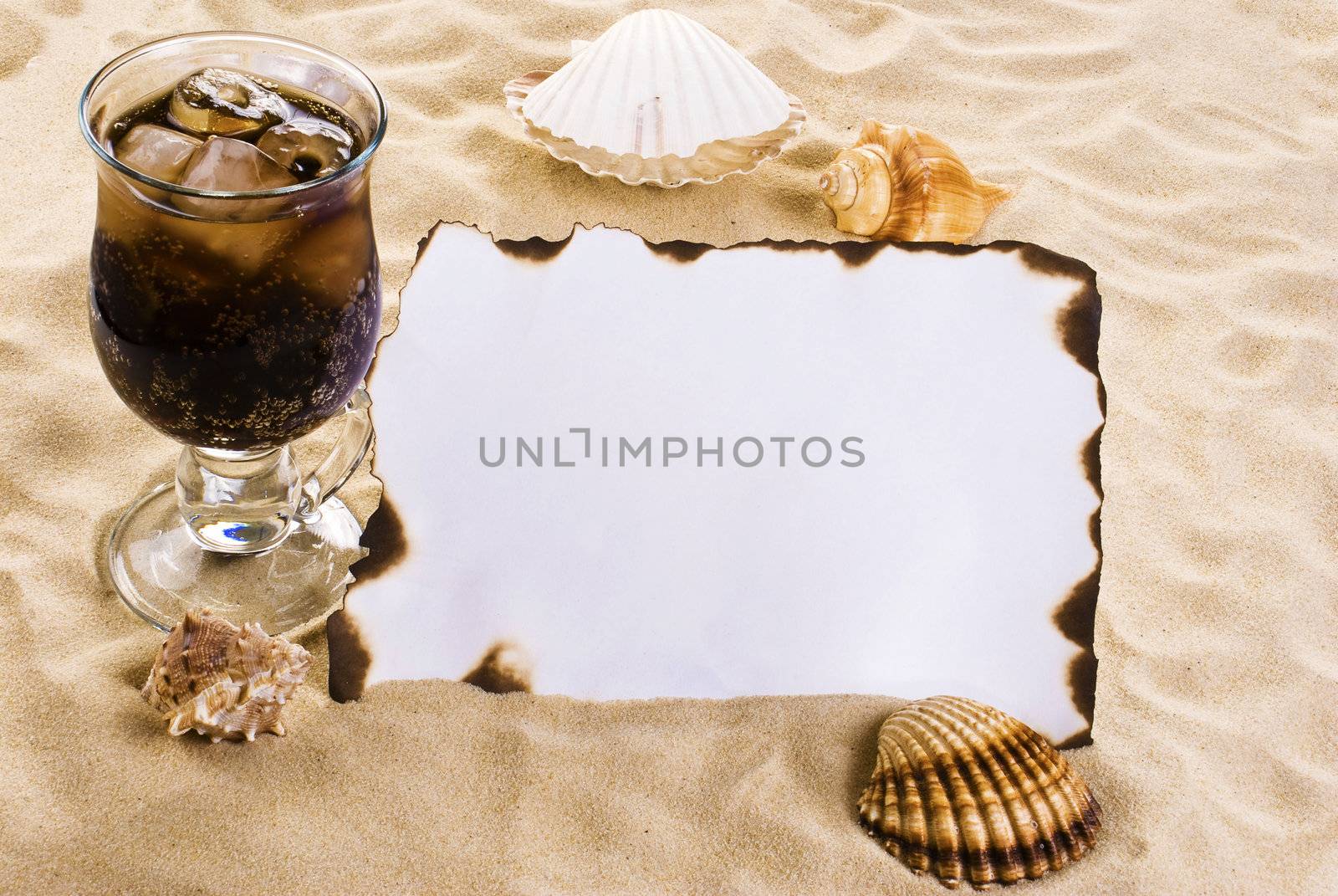 Burned paper on the sand with shells and ice cold drink