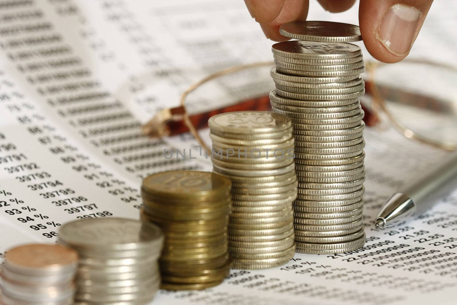 hand putting coins into a stack over a spreadsheet