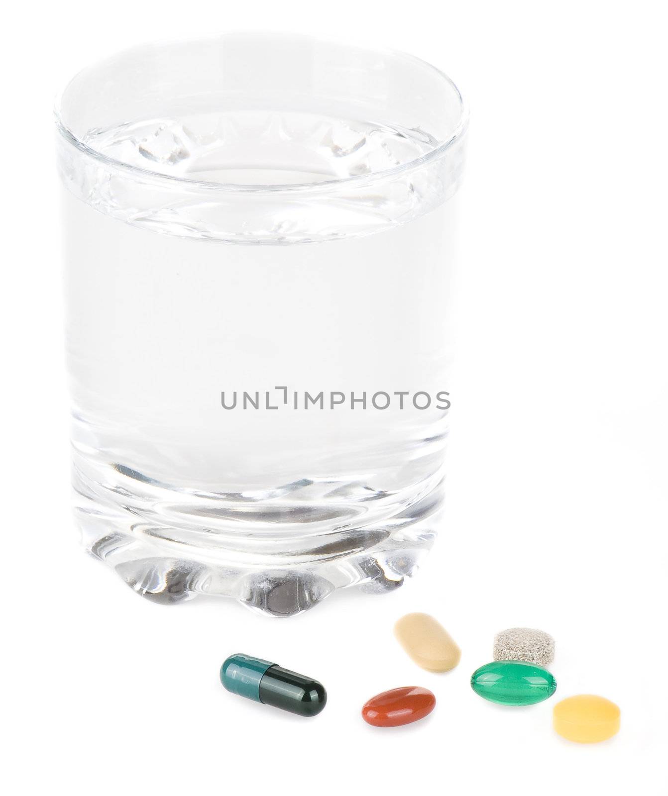 Various pills with glass of water on a white background