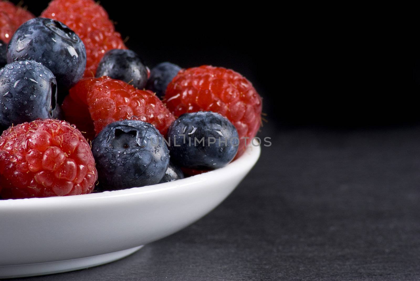 Plate of fresh blueberries and raspberries on balck background