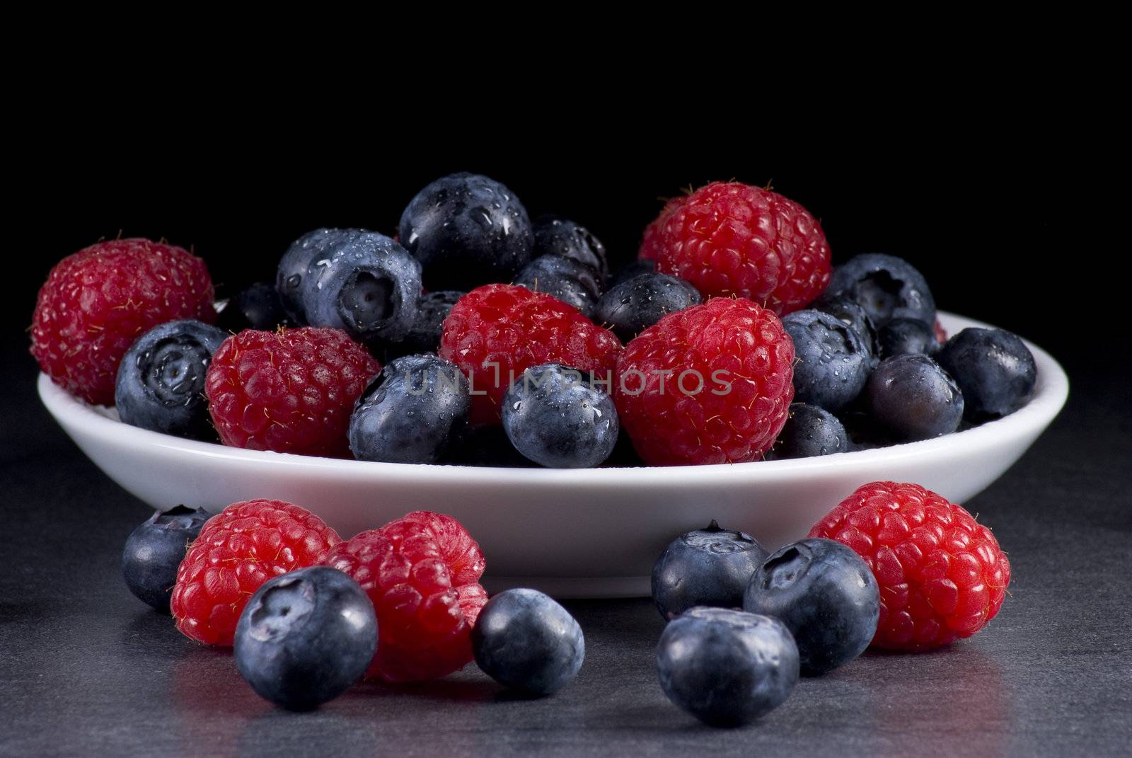 Plate of fresh blueberries and raspberries on balck background