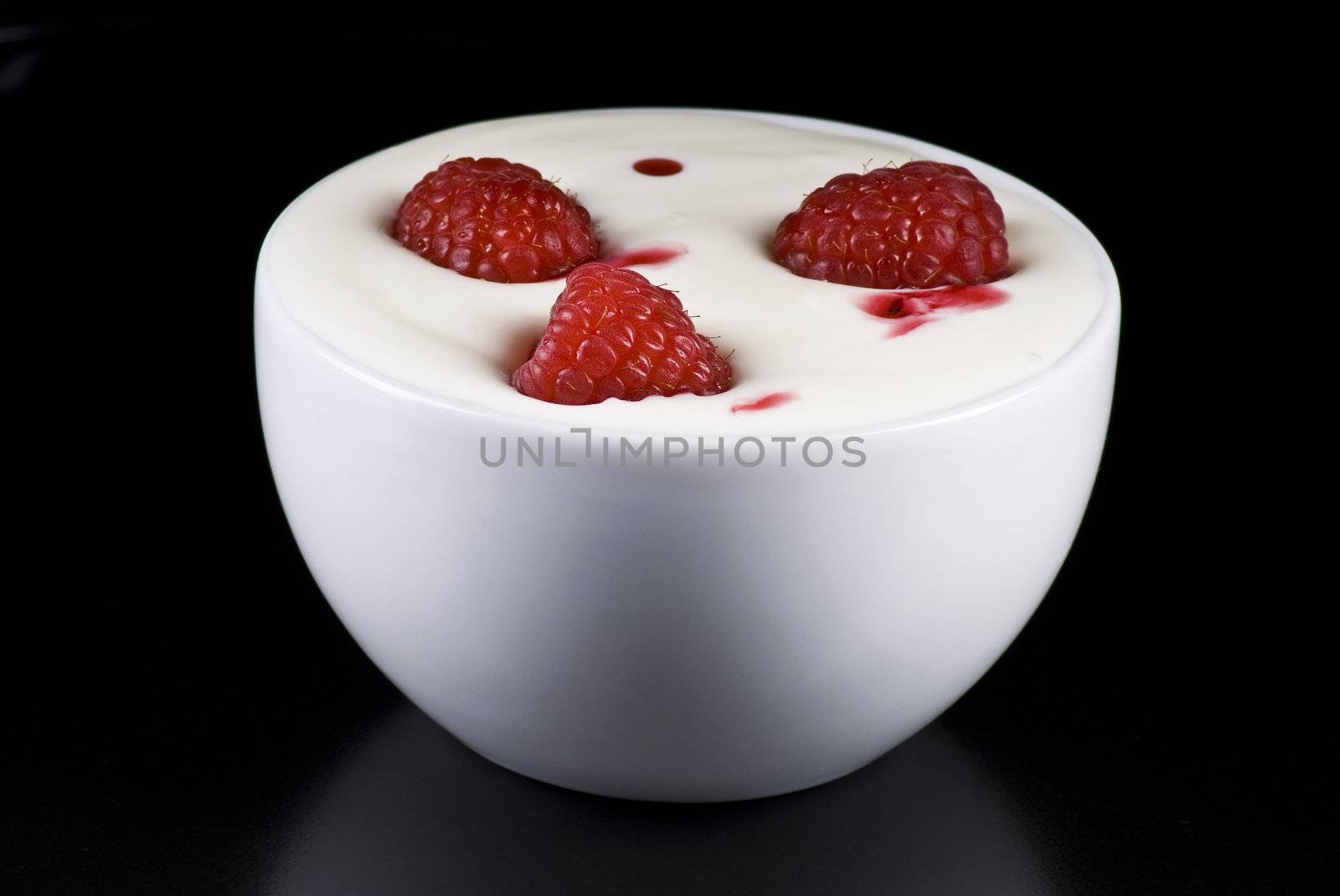 Bowl of yogurt with raspberries on black background