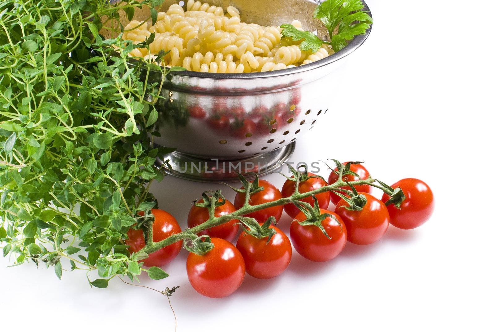 Fusilli pasta in colander with thyme and tomatoes over white background