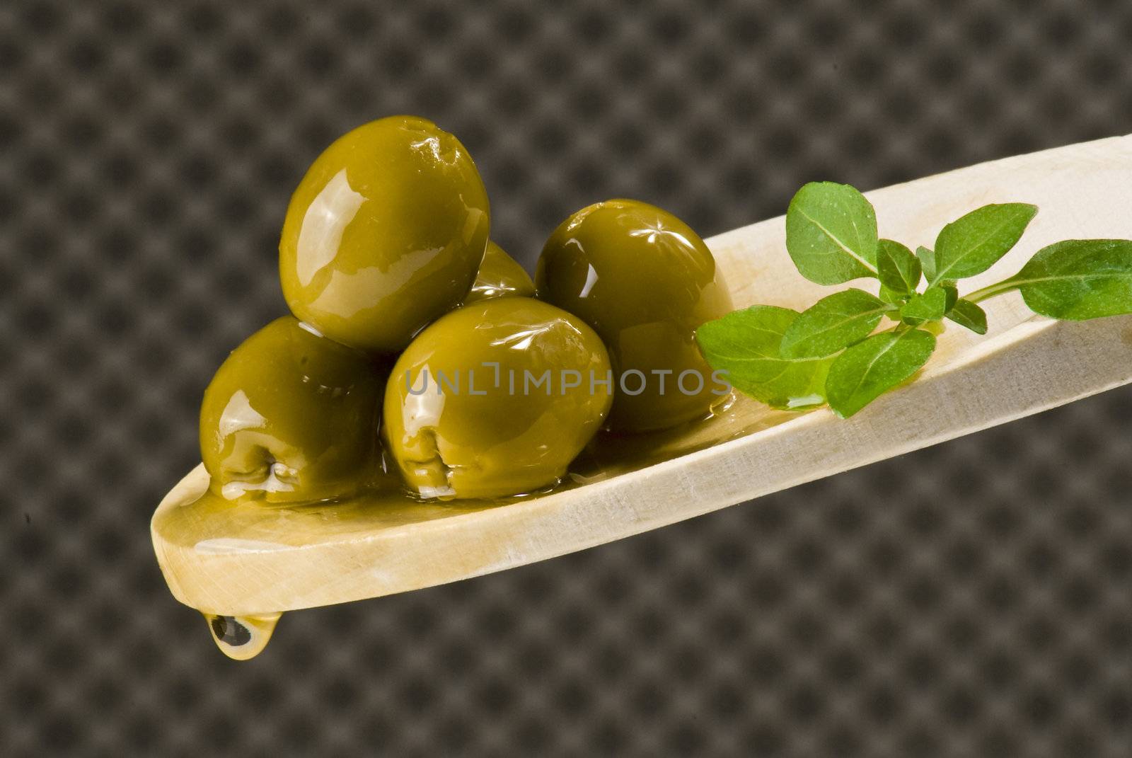 Several olives on wooden spoon over extra virgin oil