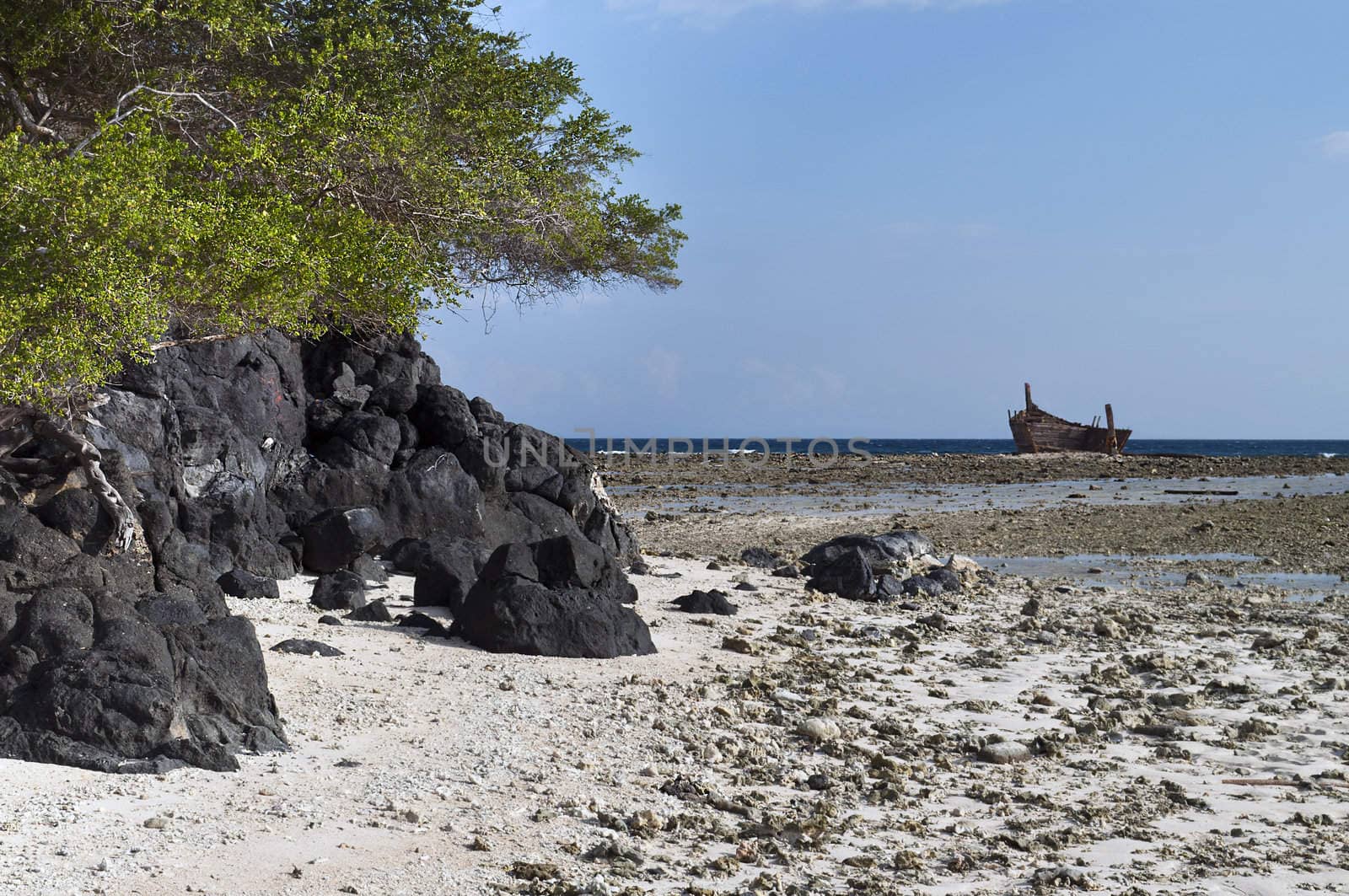 Volcanic rock in low tide shoreline with aground boat