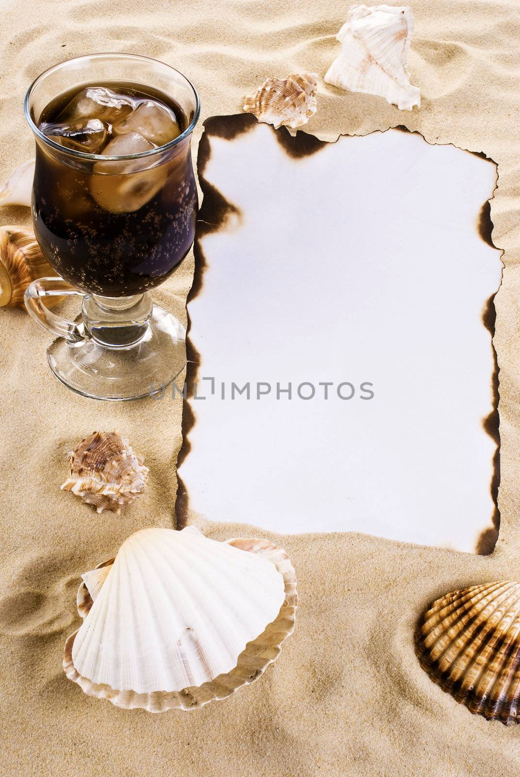 Burned paper on the sand with shells and ice cold drink