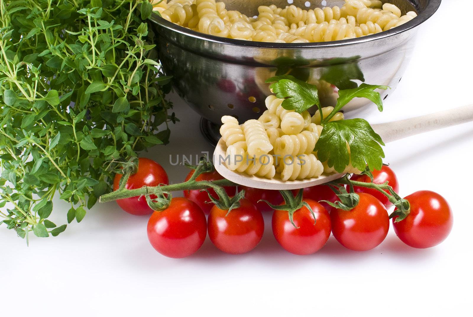 Fusilli pasta in colander with thyme and tomatoes over white background