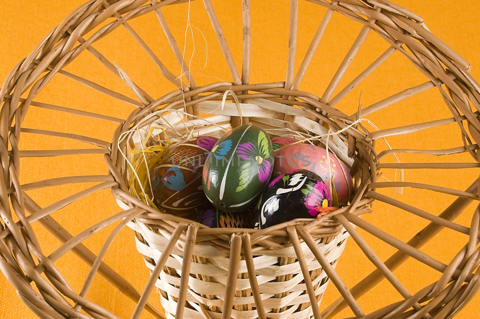 willow basket with colorful easter eggs over orange background