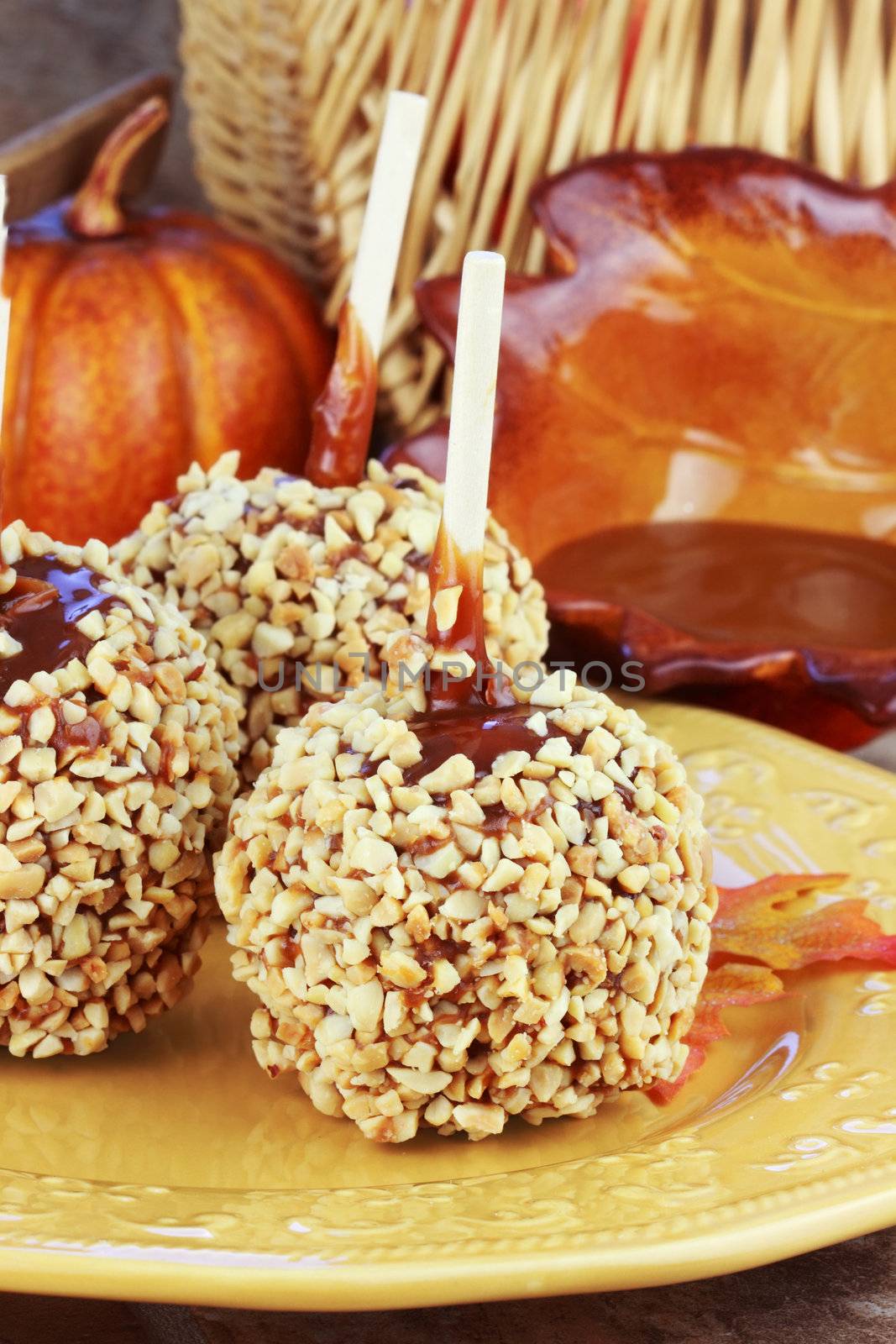 Candy apples with caramel sauce and a basket of apples in the background.