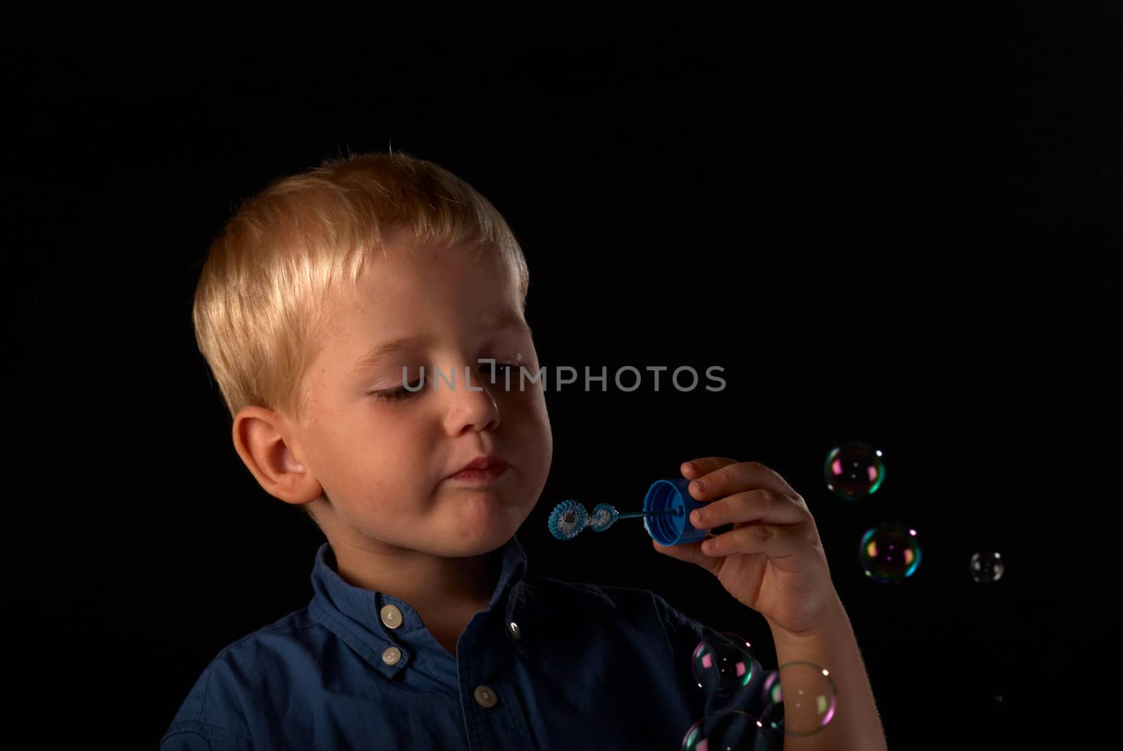 Blond boy having fun blowing colorful soap bubbles