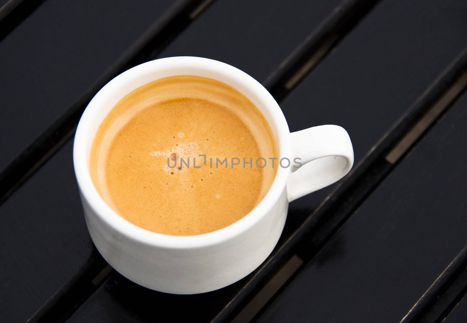 An espresso in a white cup on a dark wood table