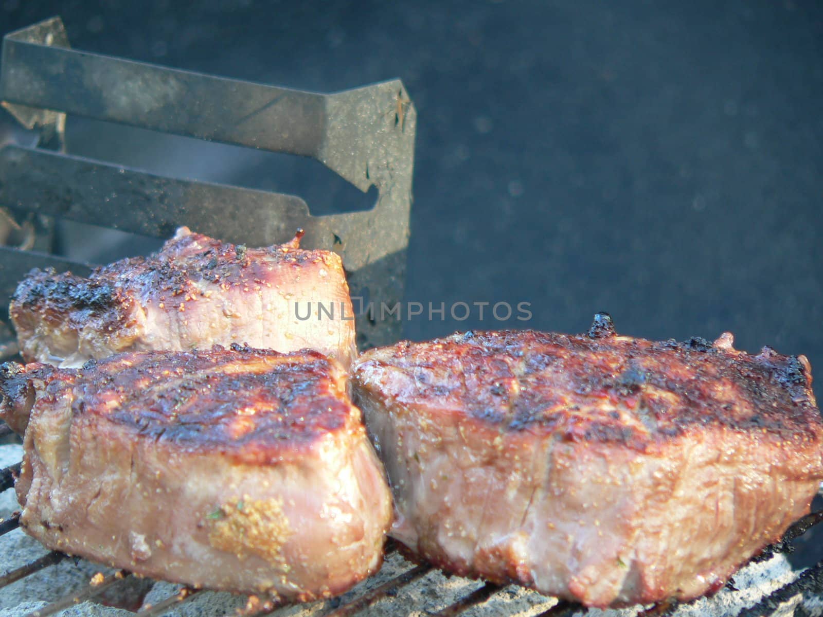 3 tenderloin steaks cooking on an charcoal grill