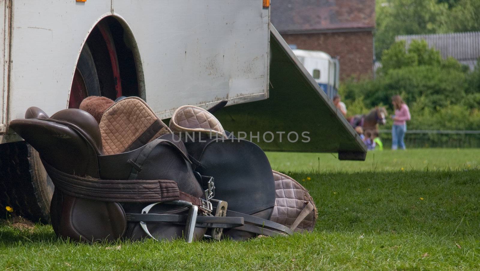 two saddles lying by a trailer at a horse event