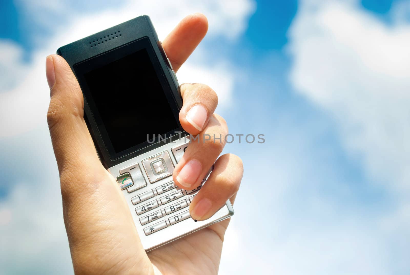 Mobile phone in hand over blue sky background. Clouds.