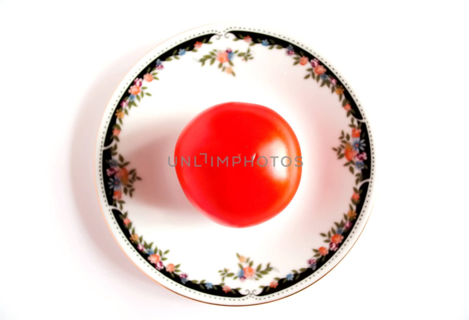 White saucer with a red tomato. by Diversphoto