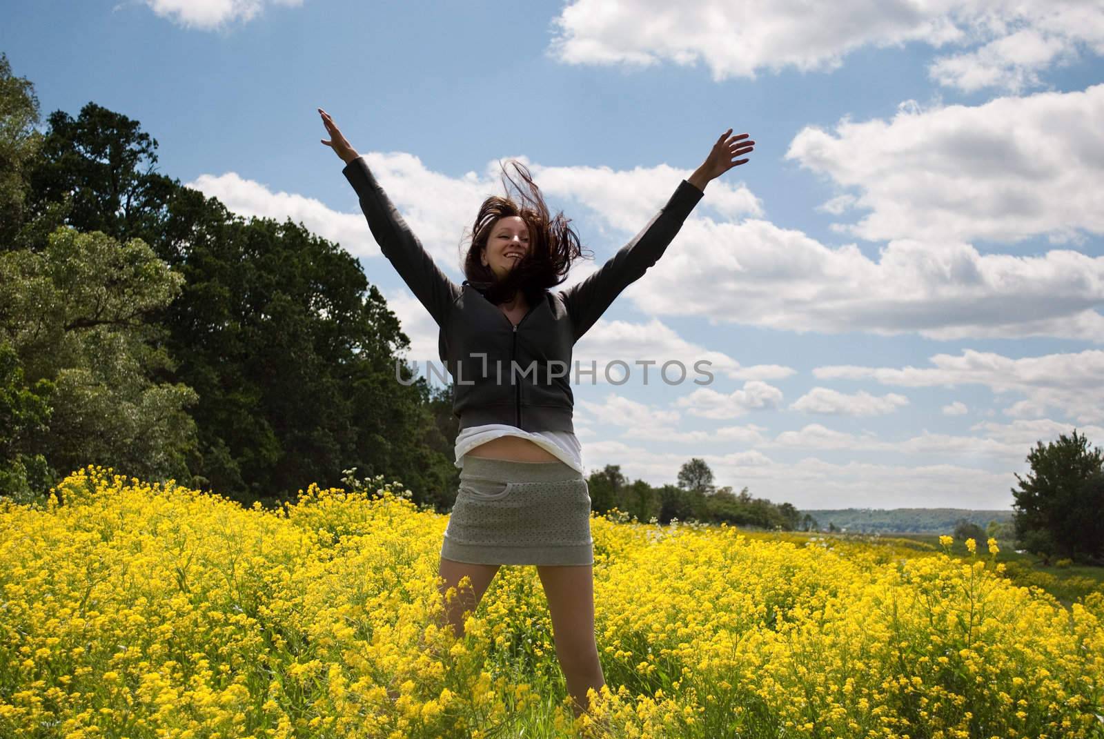 The happy girl jumps in the field of yellow flowers