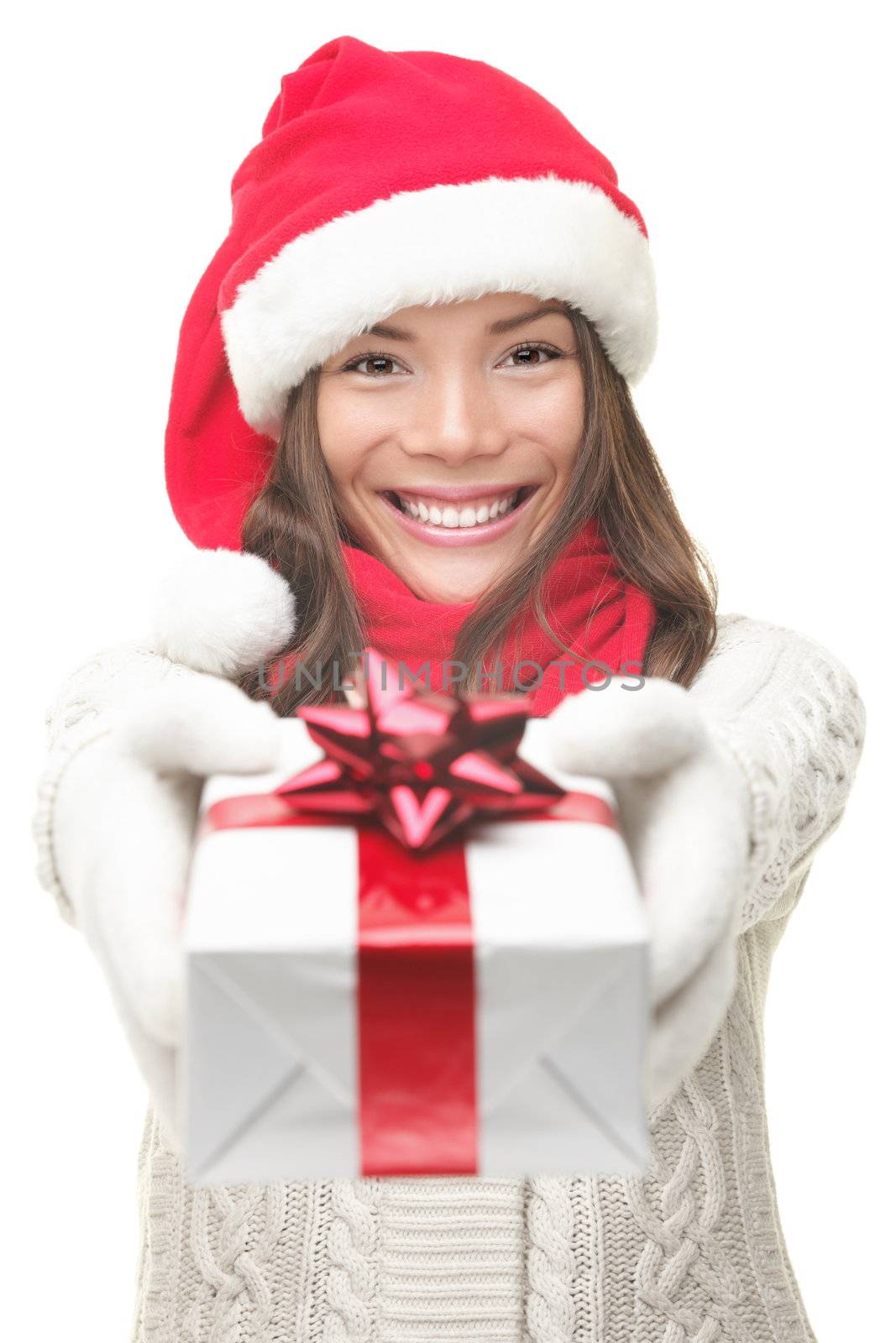Christmas gift woman smiling holding present isolated on white background. Santa girl in winter sweater showing gift wearing Santa hat. Cute, beautiful model: mixed Asian / Caucasian.
