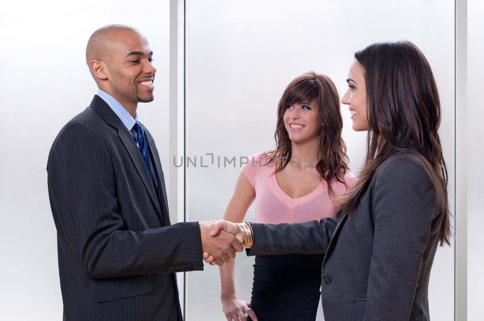 Business team of three, man and woman shaking hands and smiling.
