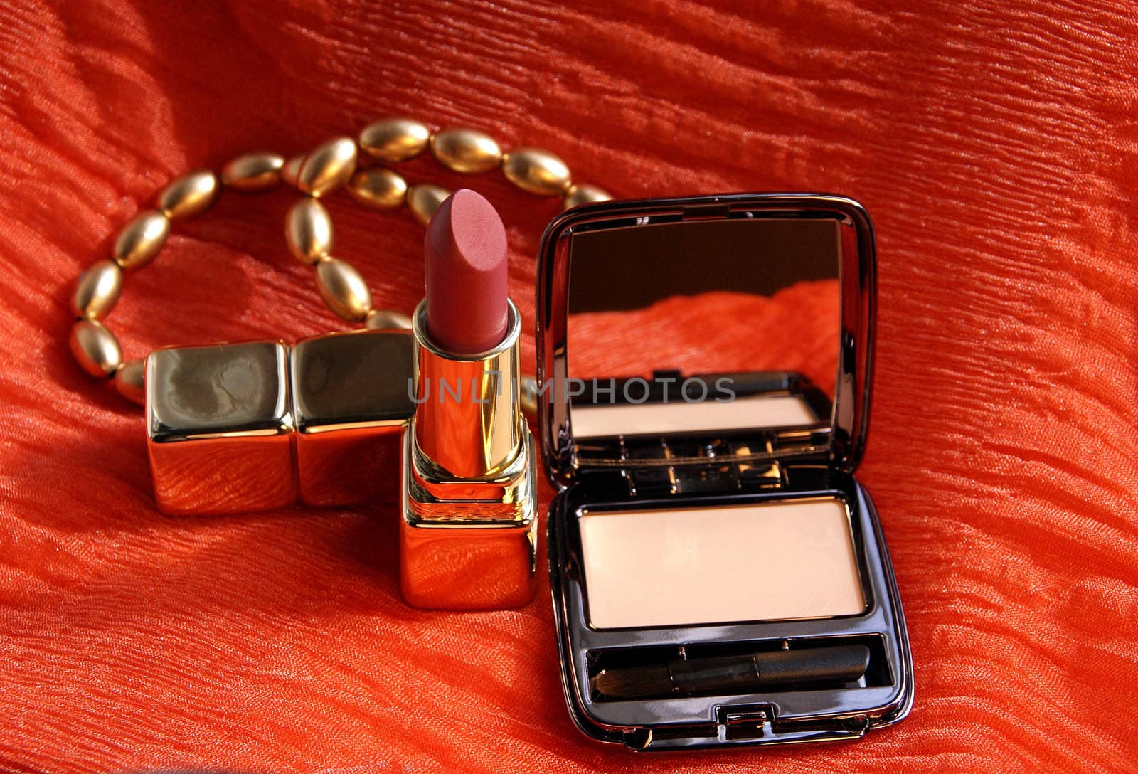 A concealer, lipstick and two fashionable bracelets over a beautiful orange scarf as background.