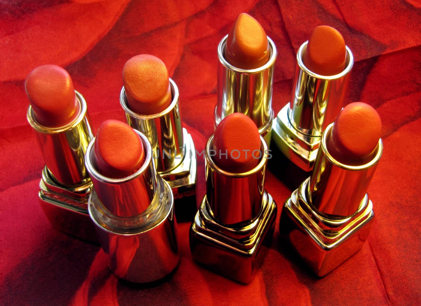 A group of seven lipsticks over a red background.