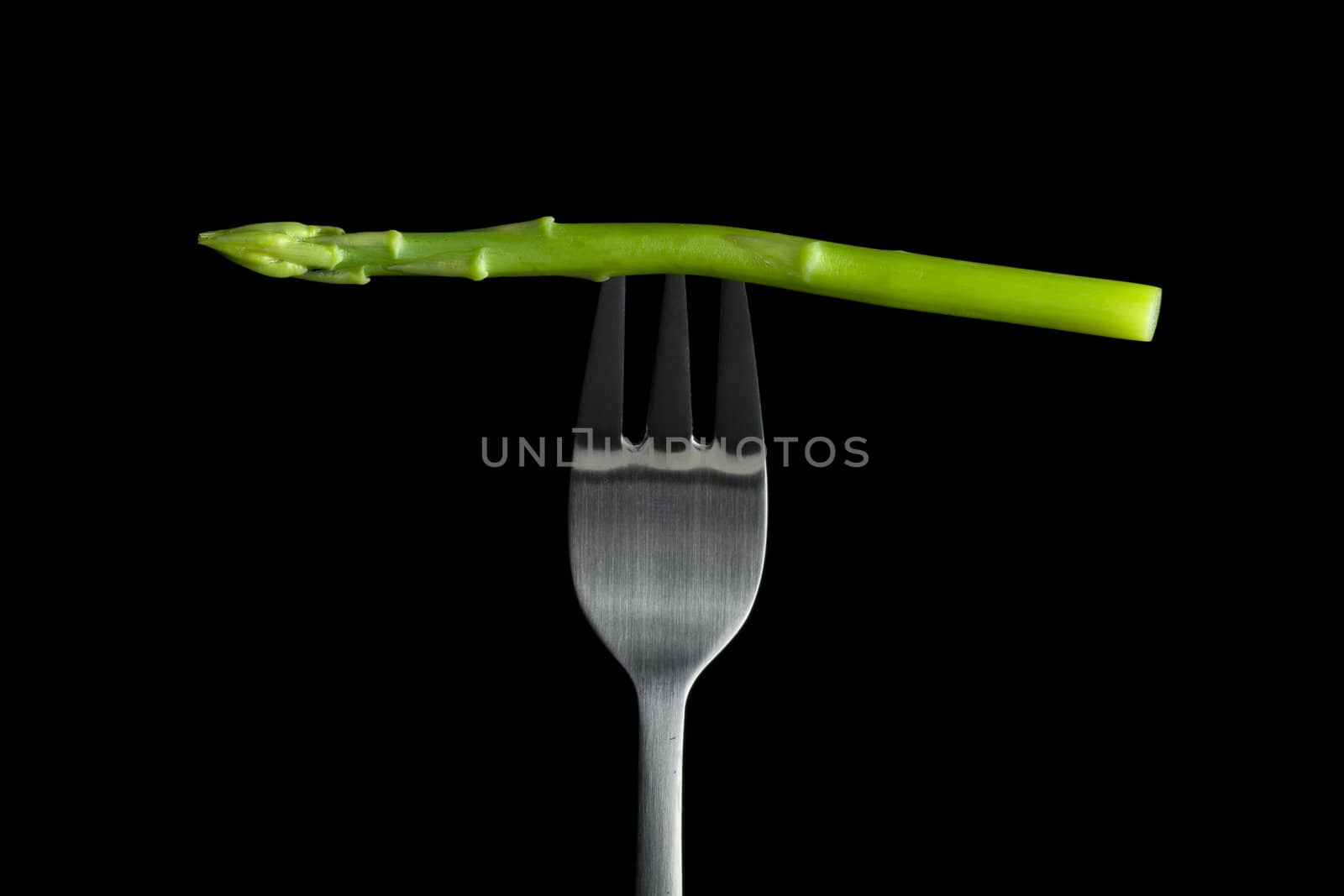 Raw asparagus on fork with black background.
