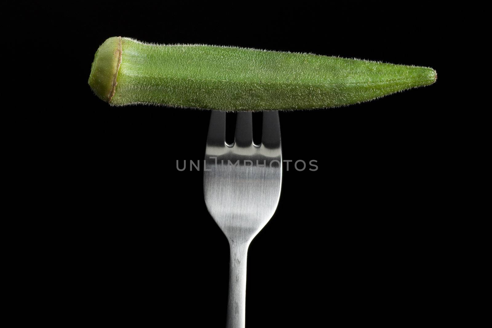 Fresh raw okra on fork with black background.